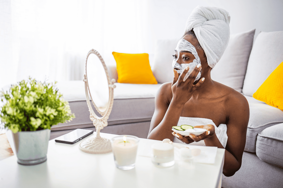 woman sitting and applying a facial mask at home while wearing a bath towel in front of the mirror