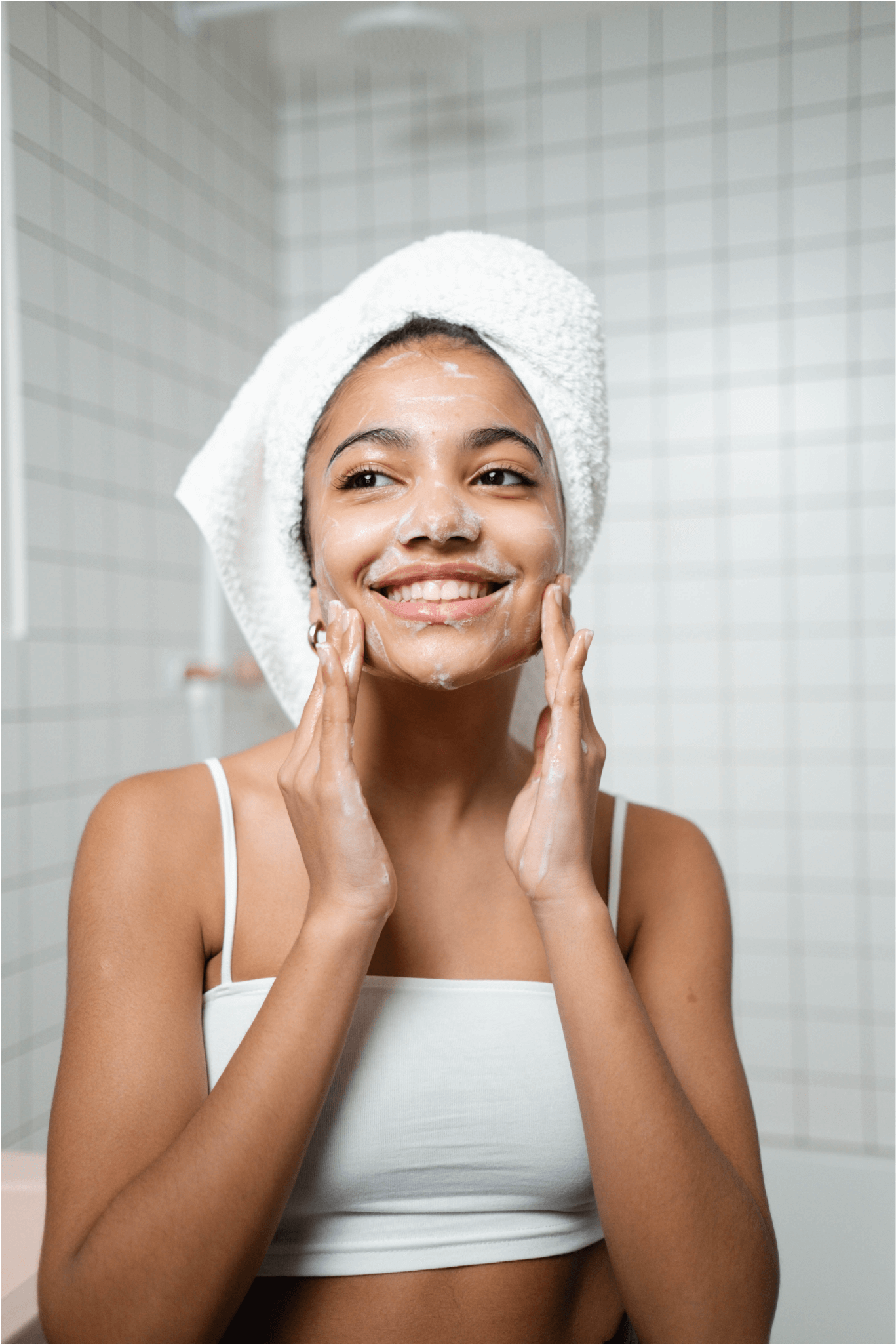 smiling young woman washing her face with healthy skin care products bath towel on her head