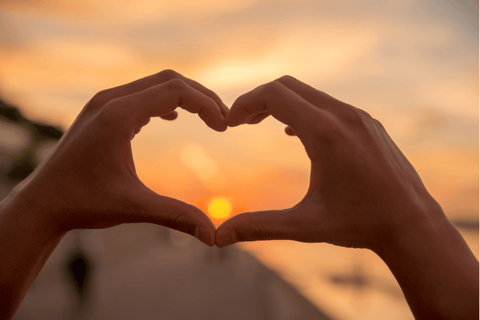 tow hands making a heart shape around a sunset