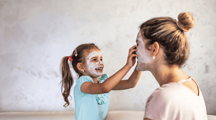 smiling girl applying a skincare mask to her mom's face