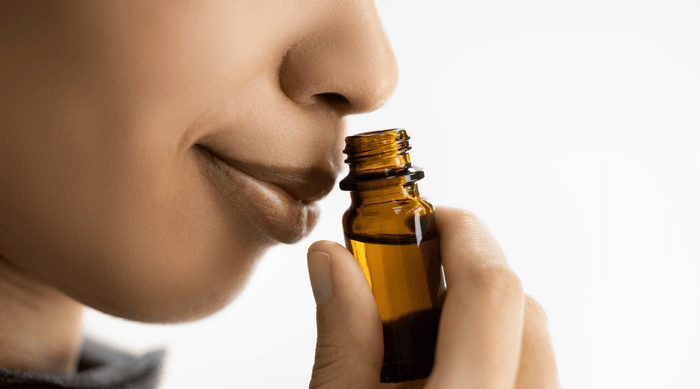 smiling woman holding a glass jar under her nose and smelling essential oils